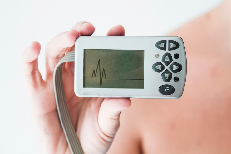 A person holds a medical device displaying an ECG heart trace.