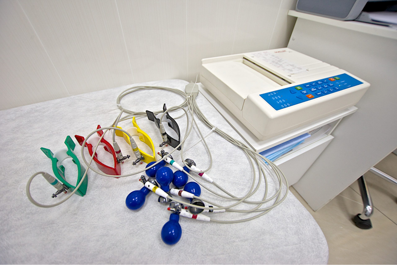 A medical device with colorful wires and electrodes placed on an examination table in a clinic.