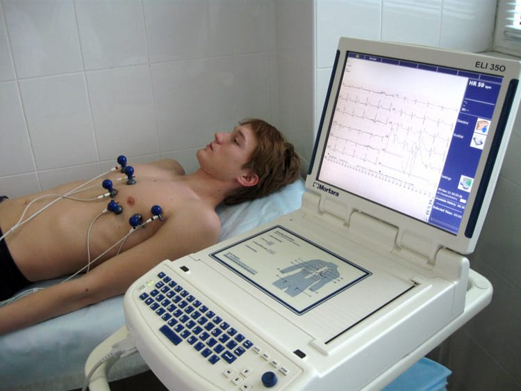 A patient undergoes an electrocardiogram (ECG) test with sensors attached to his chest and a monitor displaying the