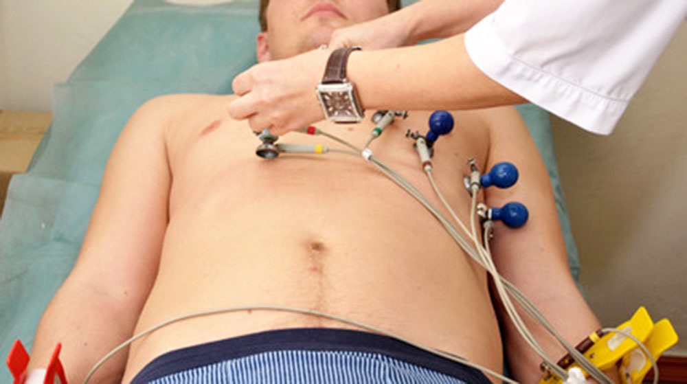 A person lies on an examination table while a healthcare professional attaches electrodes to their chest for a medical procedure.